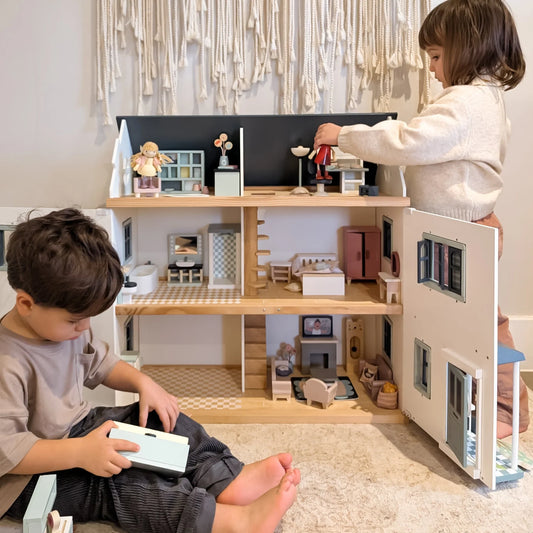 Two children playing with a wooden dollhouse in a room with decorative elements.