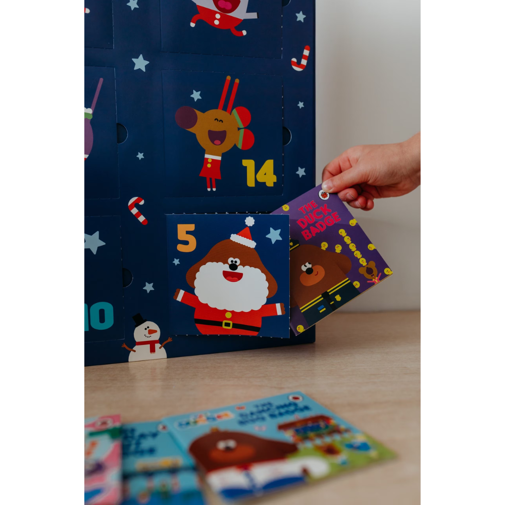 Hand opening a Christmas-themed advent calendar with cartoon characters on a wooden surface.