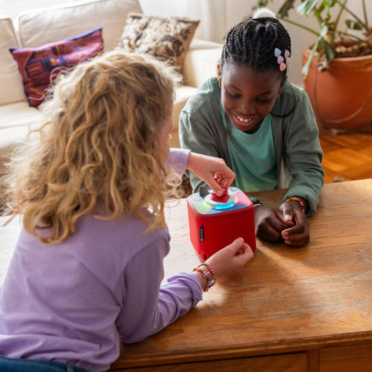 Two children playing with a colorful toy box on a wooden table.