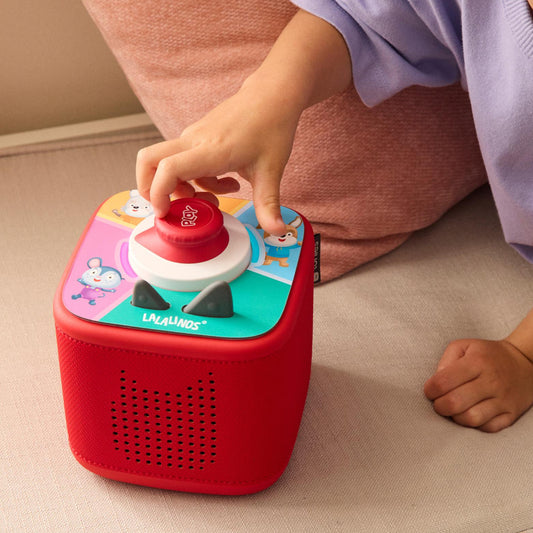 Child playing with a red toy box featuring cartoon characters on a beige surface.