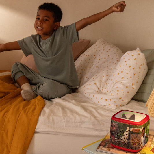 Child sitting on a bed with arms outstretched, next to a colorful nightlight