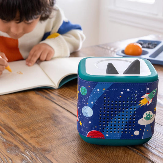 Child writing with a colorful robot-like device on a wooden table.