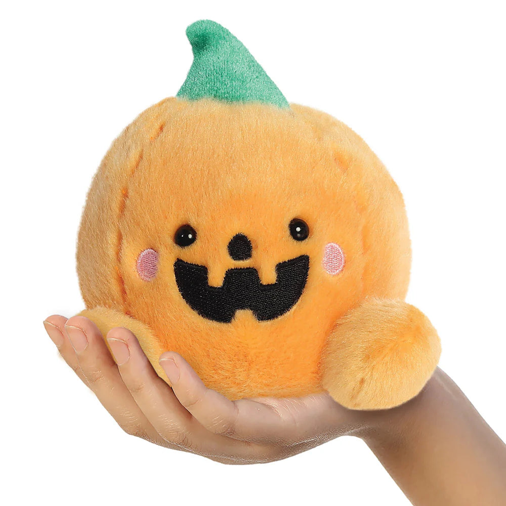 Plush pumpkin toy with a smiling face held in a hand against a white background