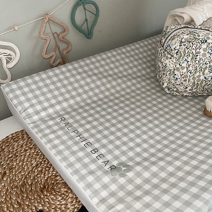 Checkered crib sheet with 'Ralphie Bear' branding on a crib, surrounded by decorative items.
