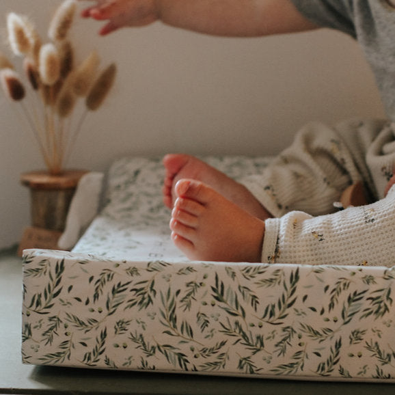Person lying on a bed with a floral-patterned mattress cover, next to a small plant.