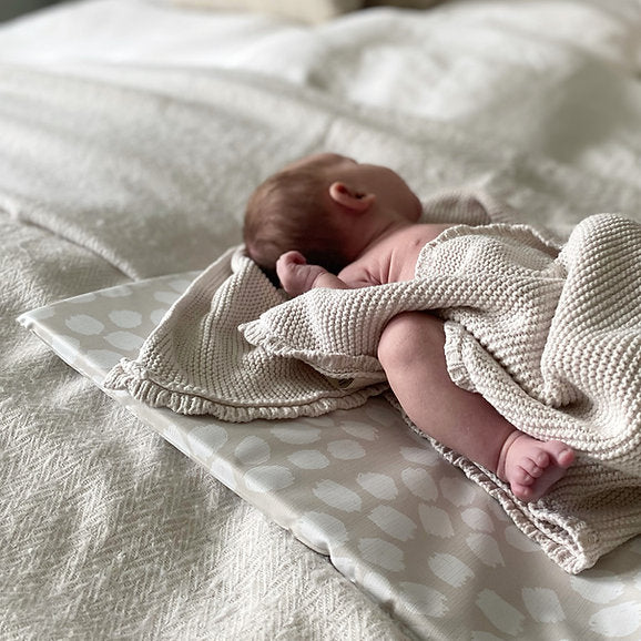 Newborn baby wrapped in a beige blanket on a textured surface