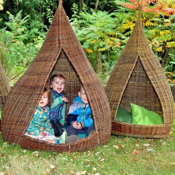 Children playing inside wicker tepee structures in a garden setting.