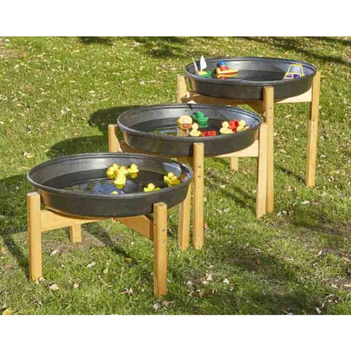 Four black metal play trays on wooden stands with toys in a grassy outdoor setting
