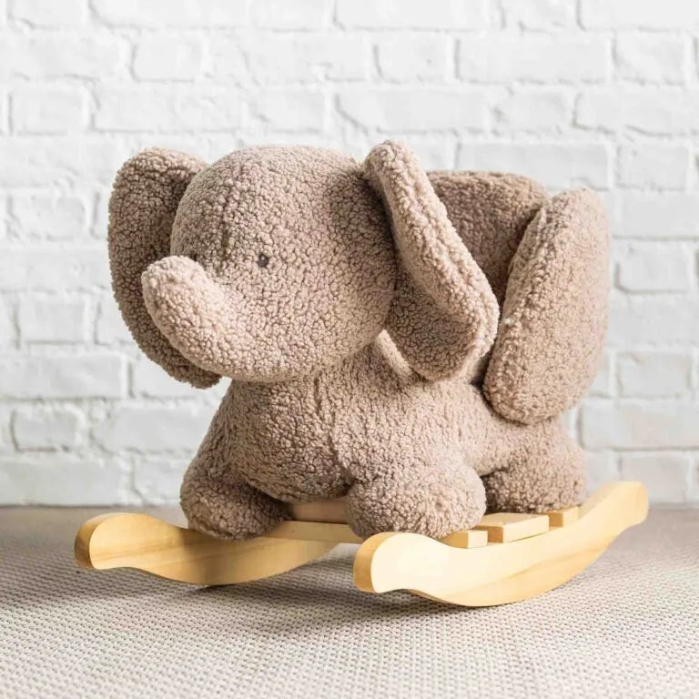 Plush rocking elephant toy against a white brick wall.