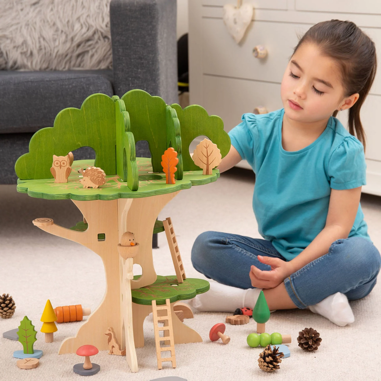 Child playing with a wooden treehouse toy set on the floor.