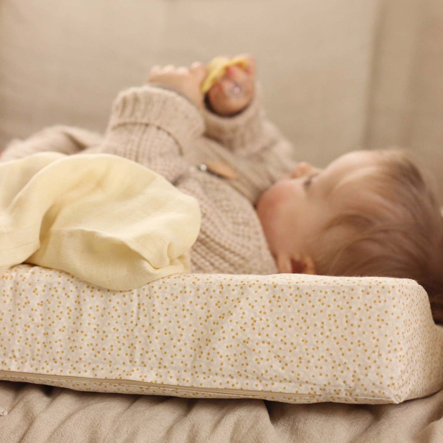Baby lying on a changing table with a yellow blanket and toy