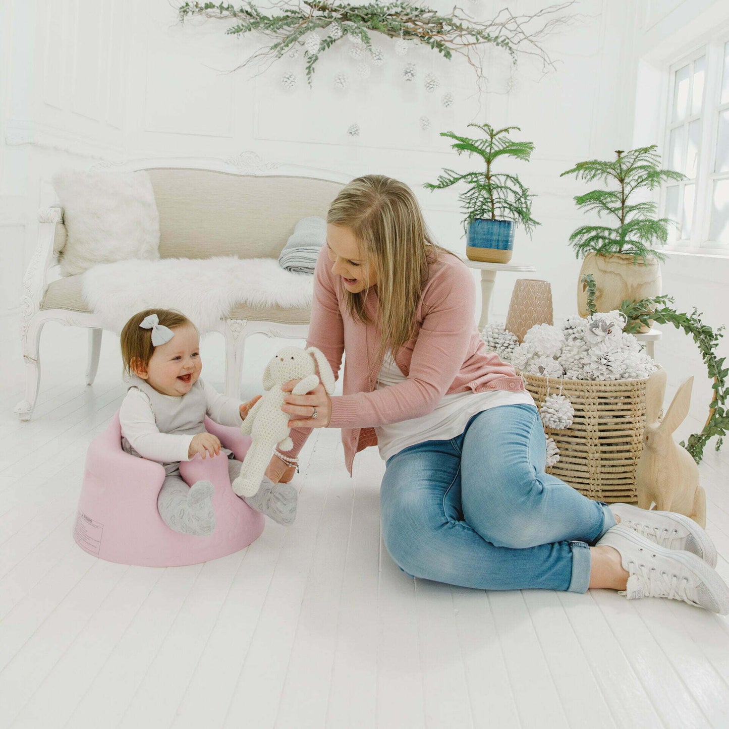 Woman and child in a cozy living room with plants and a pink chair.