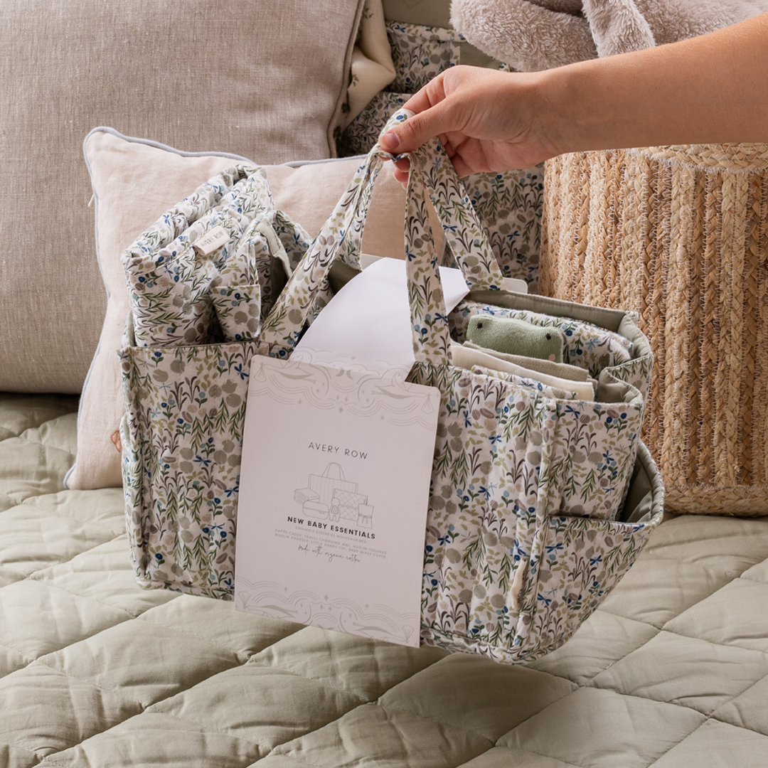Floral-patterned baby organizer held by a hand on a bed with pillows and blankets.