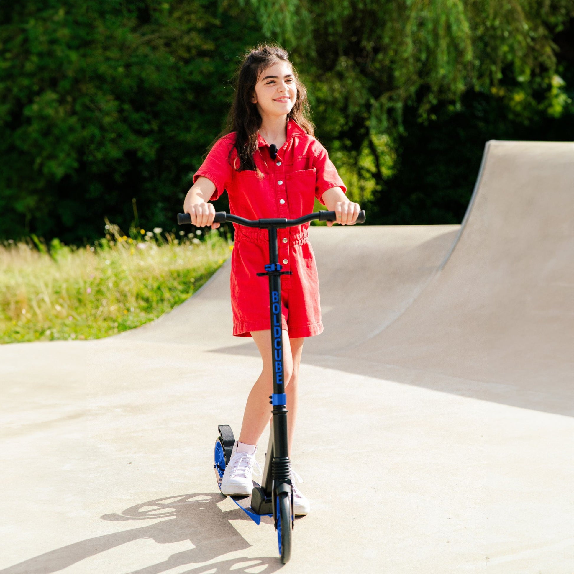 Girl in a red dress riding a scooter at a skate park.