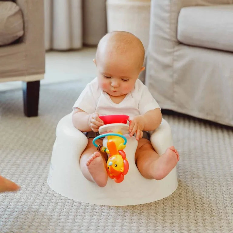 Baby sitting on a white stool with colorful toys in a living room.