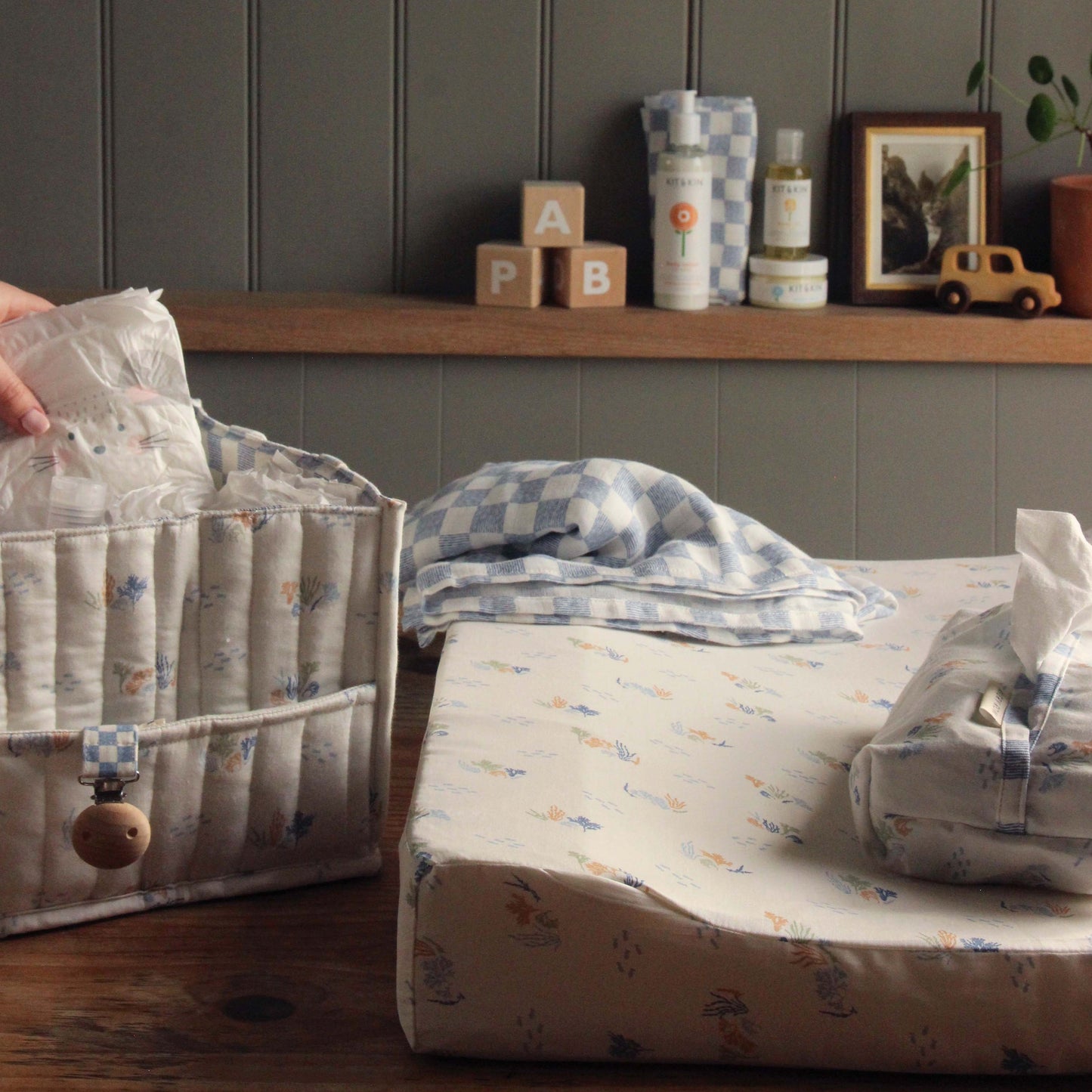 Baby changing area with patterned diaper bag, changing mat, and baby products on a shelf.