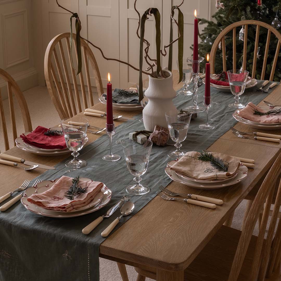 Dining table set for a meal with place settings, candles, and a Christmas tree in the background.