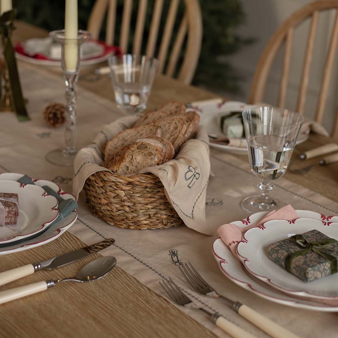 Dining table set with bread basket, plates, and cutlery on a wooden table.