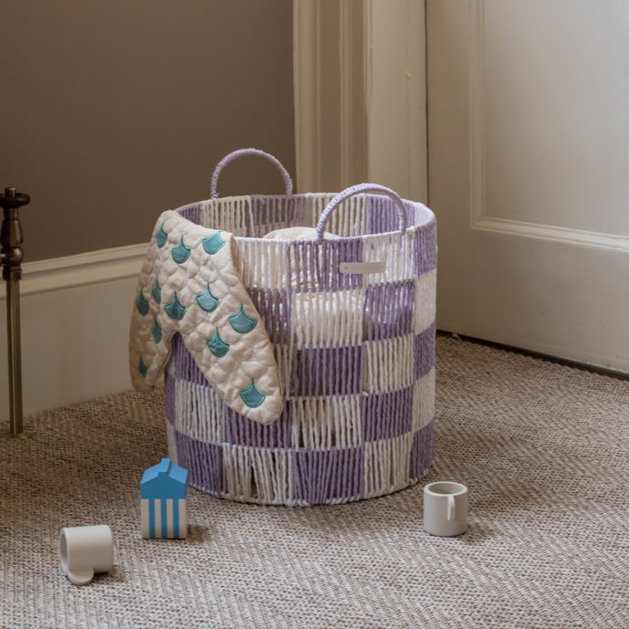 Checkered laundry basket with a quilted cover on a carpeted floor