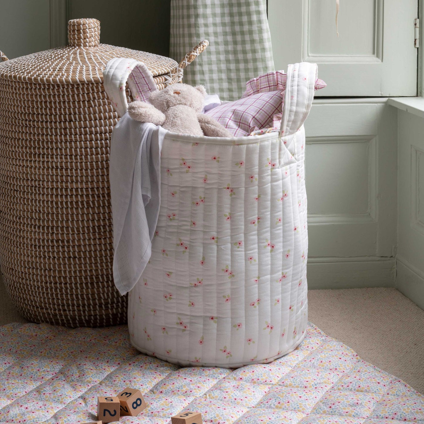 White floral-patterned laundry basket with toys and a wicker basket in a room.