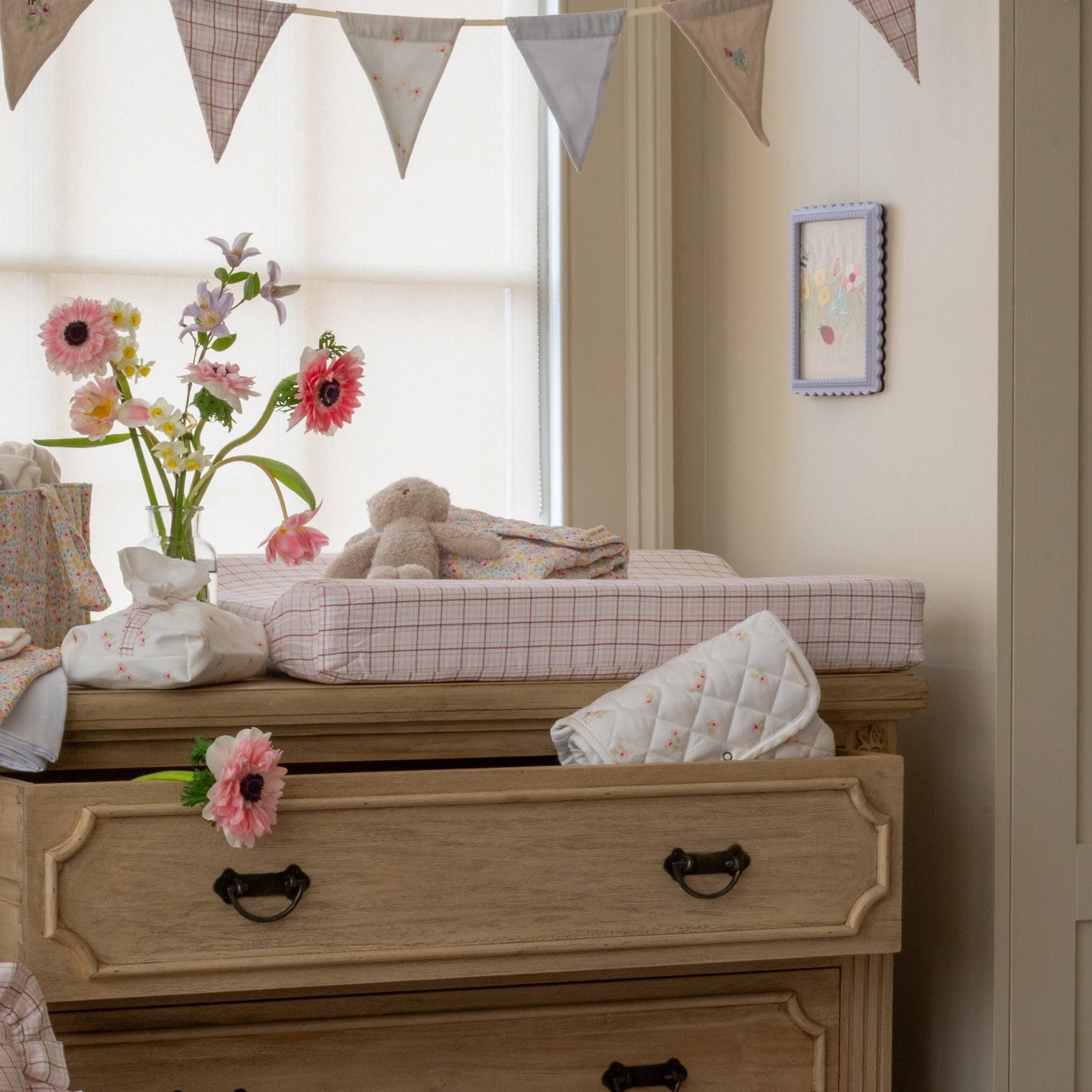 Nursery room with wooden dresser, flowers, and toys.