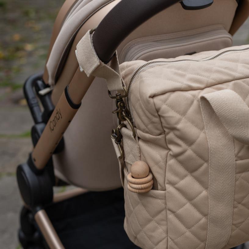 Beige quilted bag attached to a stroller with a blurred background