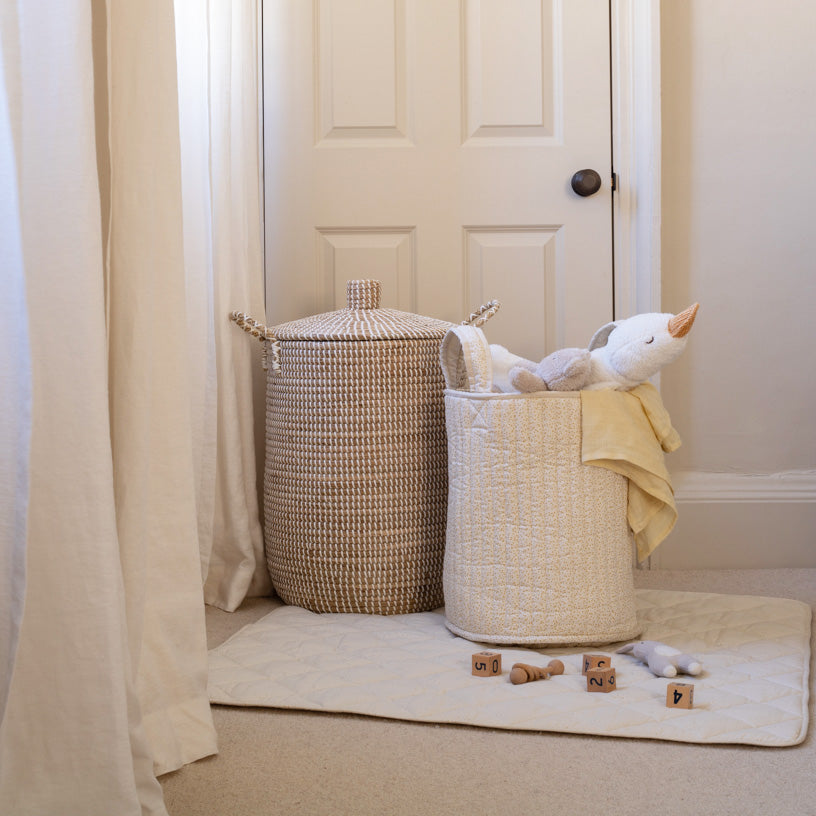 Two laundry baskets with toys and clothes in a room with a white door and beige carpet.
