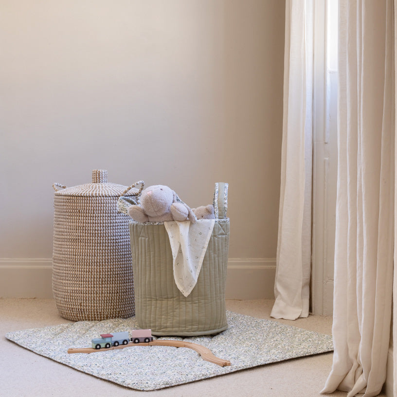 Children's toys and a basket on a rug in a room with neutral walls and curtains.