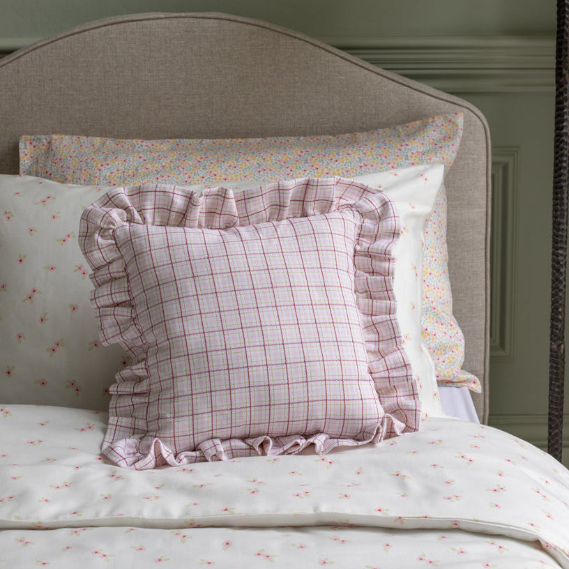 Checkered pillow with ruffles on a bed with floral and checkered pillows.