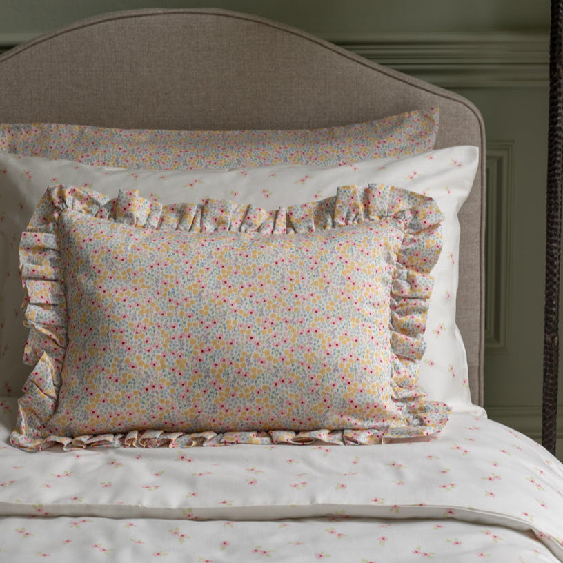 Floral patterned pillow with ruffles on a bed with matching bedding.