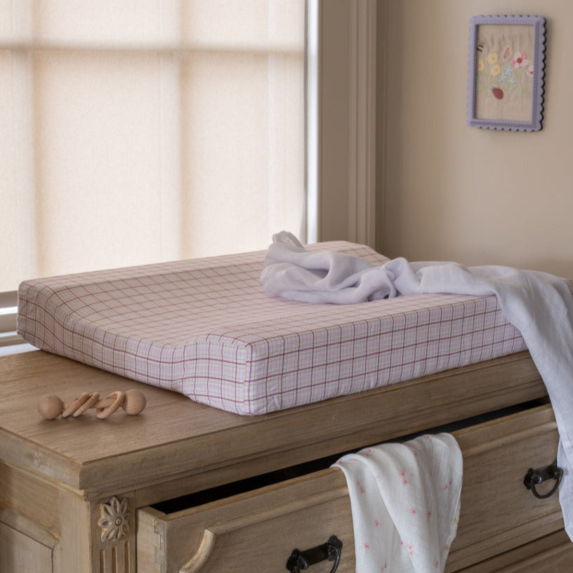 Wooden changing table with checkered pad and baby items in a room setting