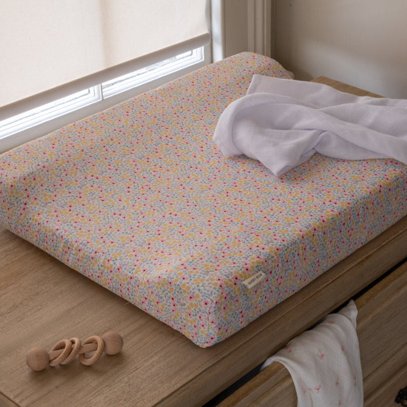 Floral-patterned changing pad on a wooden changing table with a white towel and wooden toy.