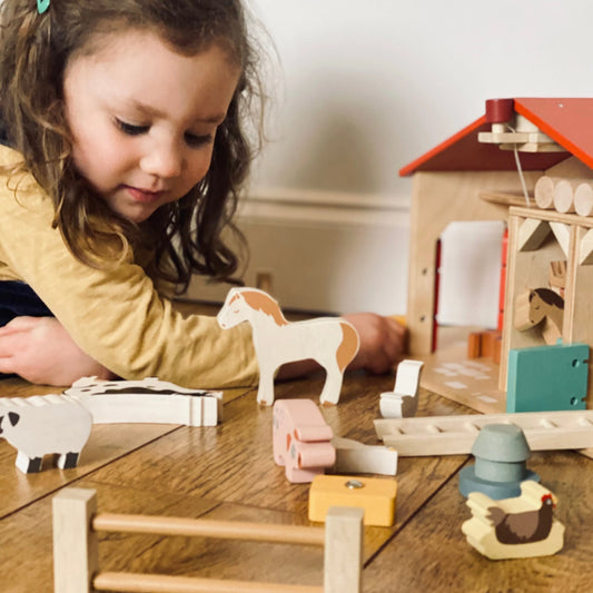 Child playing with wooden farm toys on a table