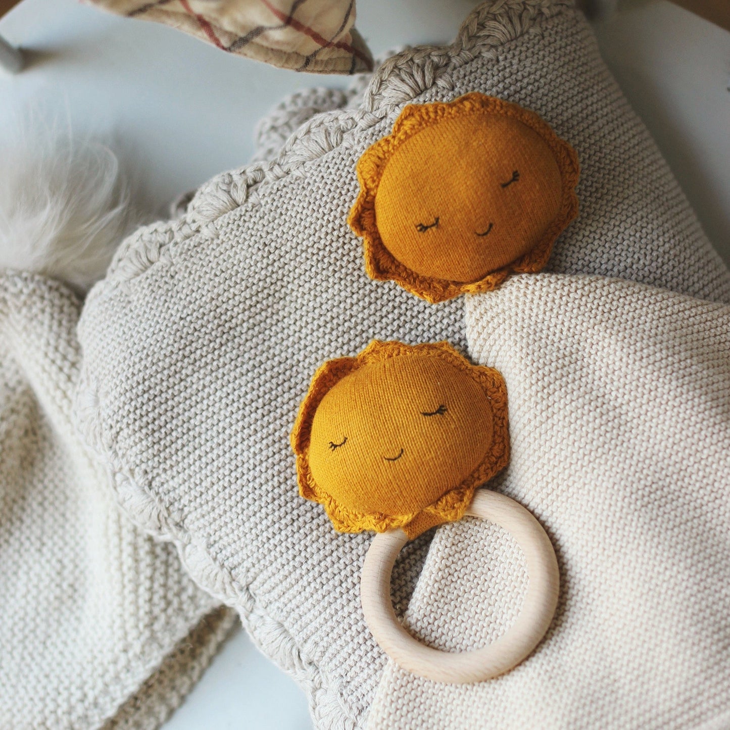 Two mustard yellow lion-shaped toys with wooden rings on a textured fabric surface.