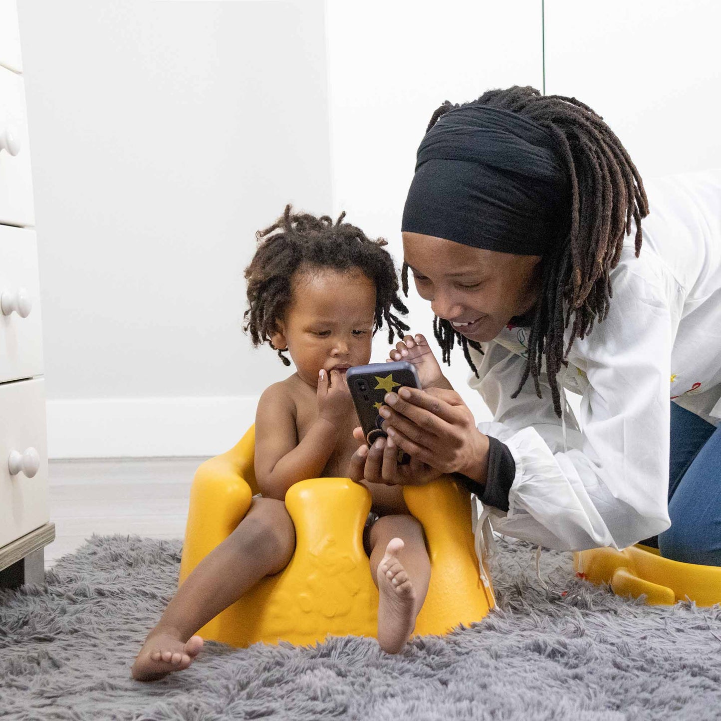 Woman and child using a smartphone together on a gray carpet
