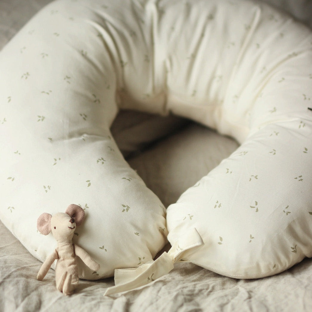White U-shaped pillow with small green patterns on a soft surface, accompanied by a plush toy mouse.
