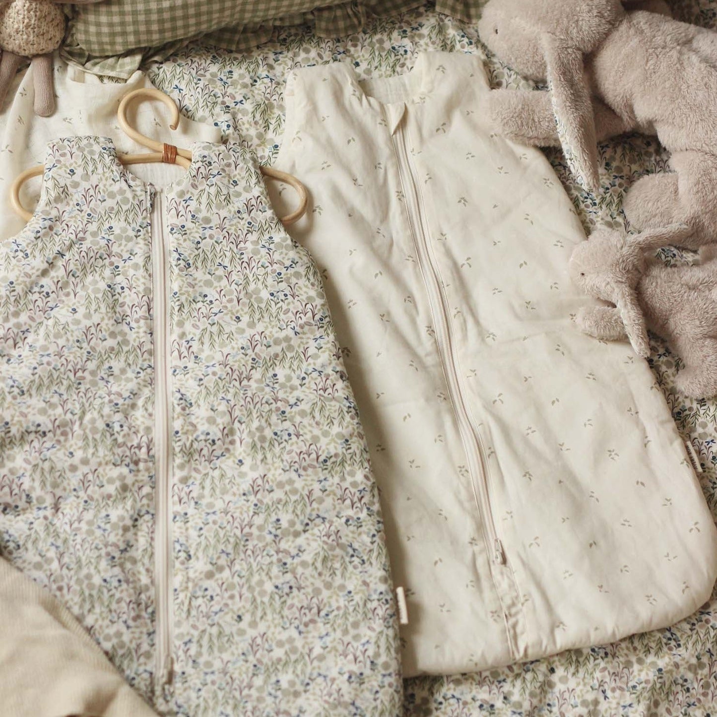 Two baby outfits on a textured surface with a soft blanket and plush toy.