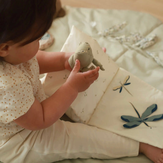 Child holding a soft toy on a bed with embroidered dragonflies
