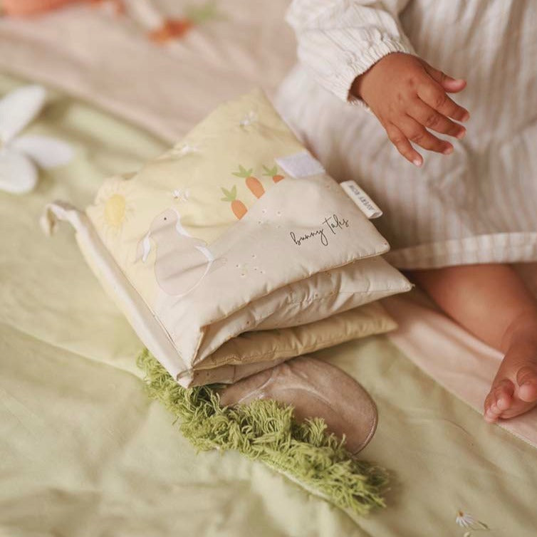 Stack of baby blankets with a child's hand reaching towards them on a soft surface.