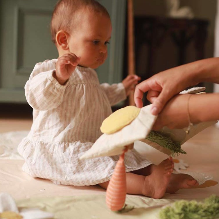 Baby playing with a toy carrot on a bed