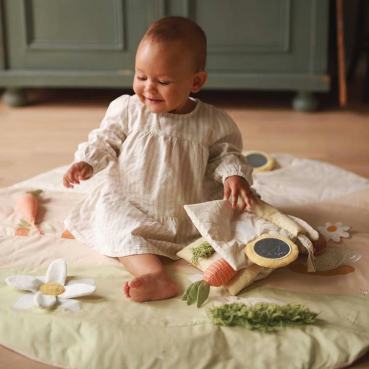 Baby in a white dress sitting on a blanket with toys