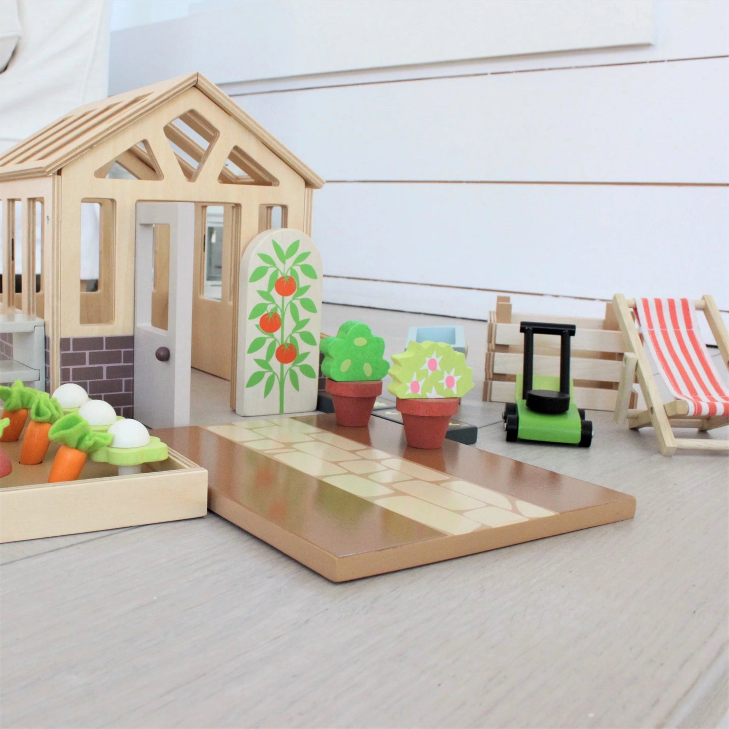 Wooden toy set with a house, garden, and furniture on a light surface.