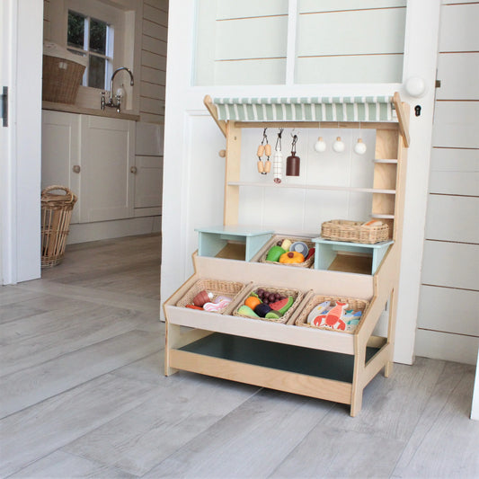 Children's play kitchen set with shelves and toy food on a wooden floor.