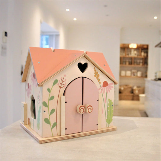 Wooden toy house with pink roof and floral decorations on a white surface.