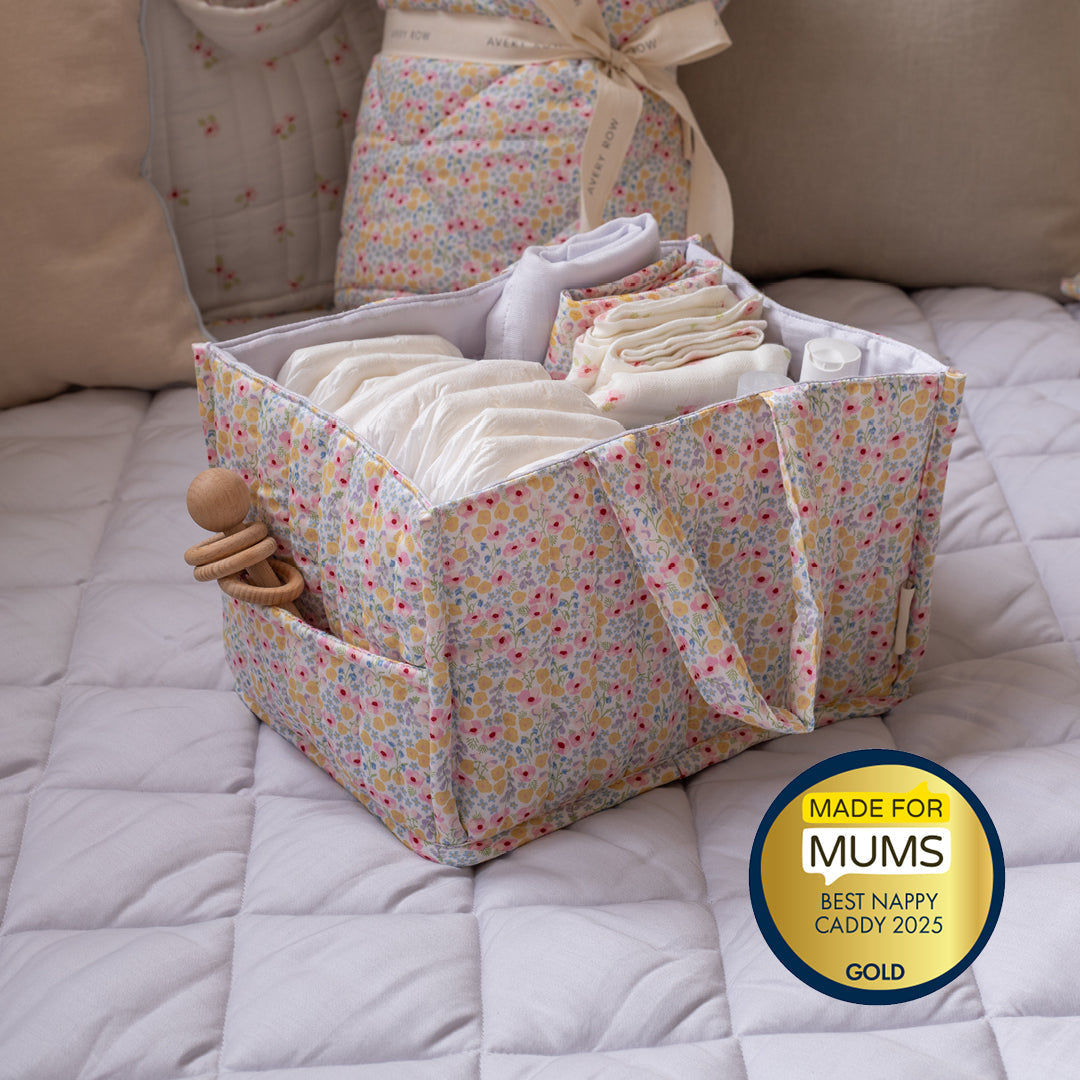 Floral-patterned nappy caddy with baby items on a bed, featuring a 'Made for Mums' award badge.