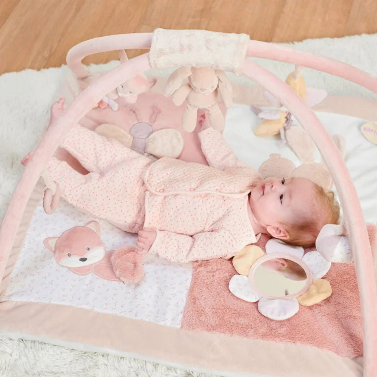 Baby lying on a pink play mat with toys and a baby gym