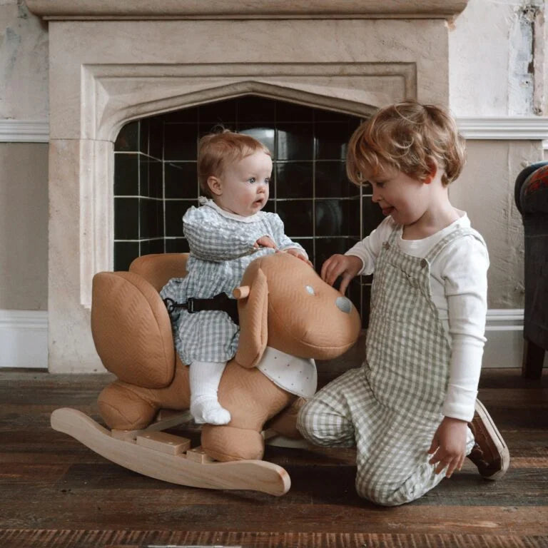 Two children playing with a rocking horse in a cozy room.