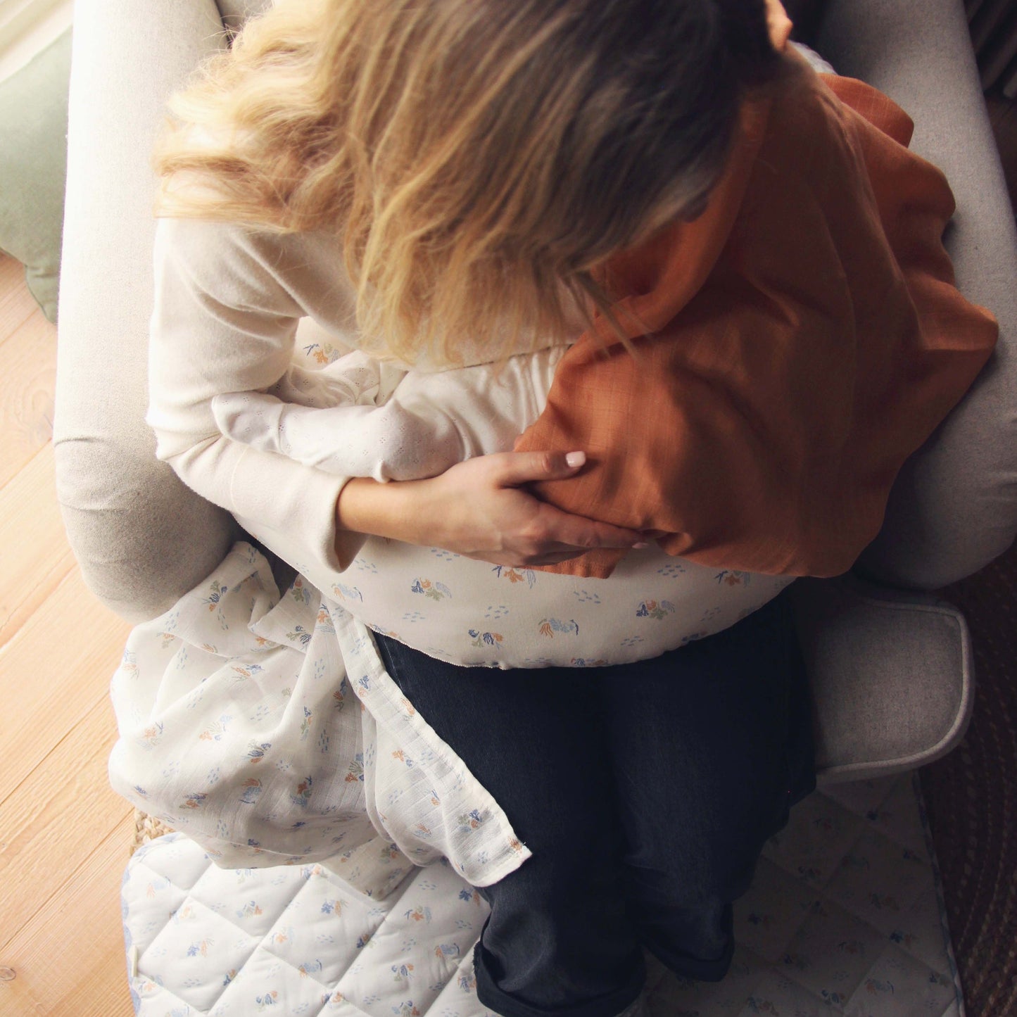 Two people sitting close together on a couch, one wearing an orange hoodie and the other in a white patterned dress.