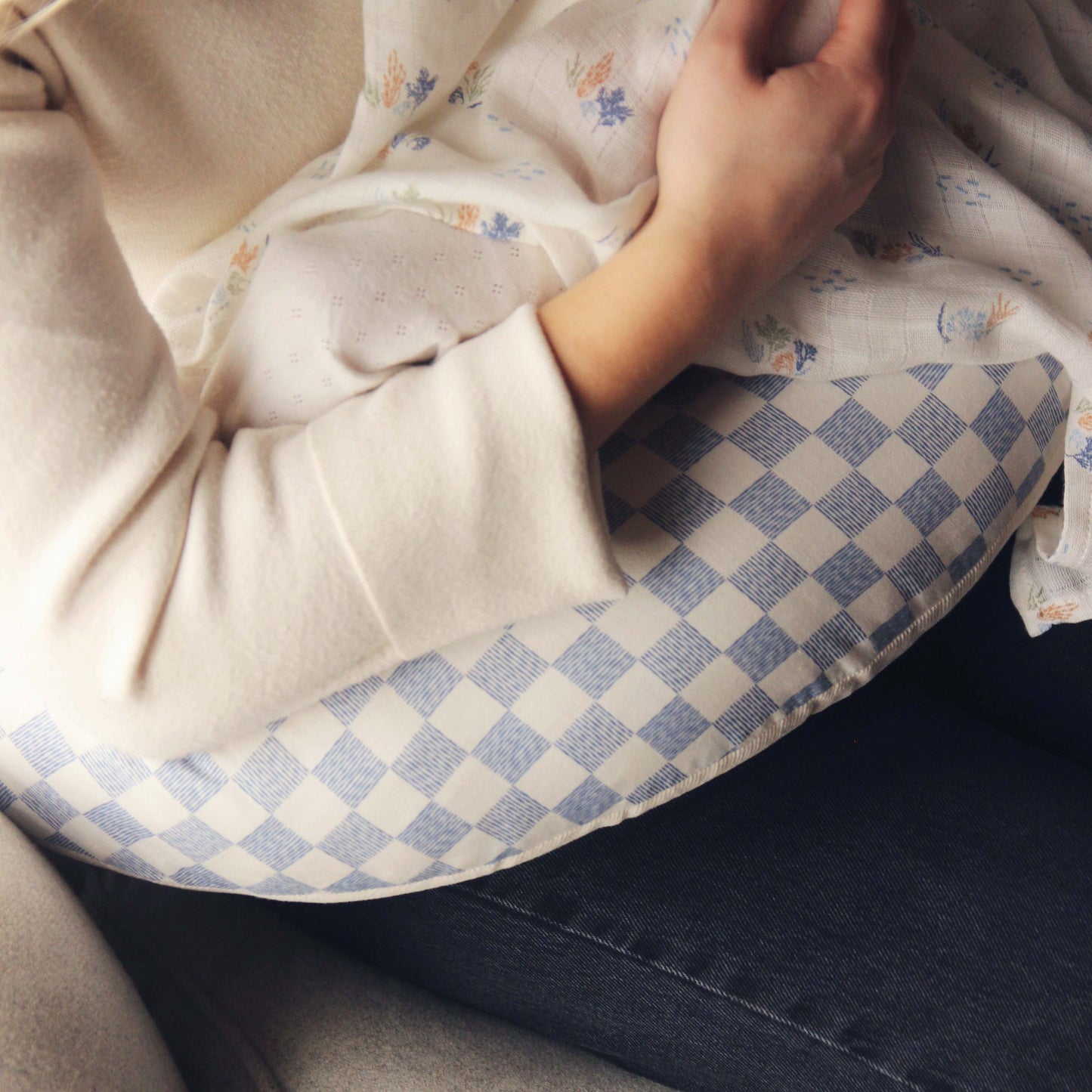 Person lying on a checkered pillow with a floral blanket, wearing a beige sweater.