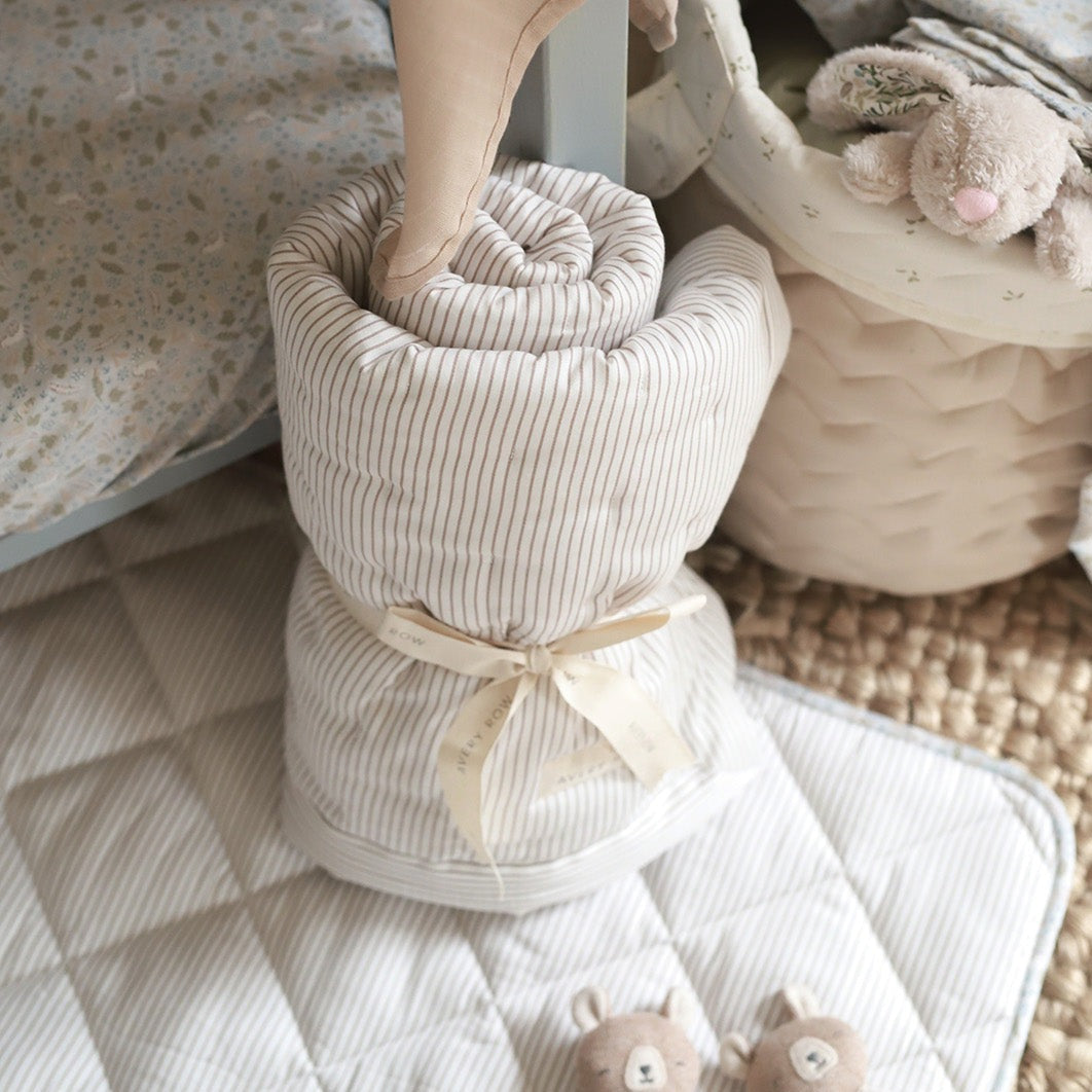 Folded striped towel with a ribbon, placed on a textured surface with soft toys in the background.
